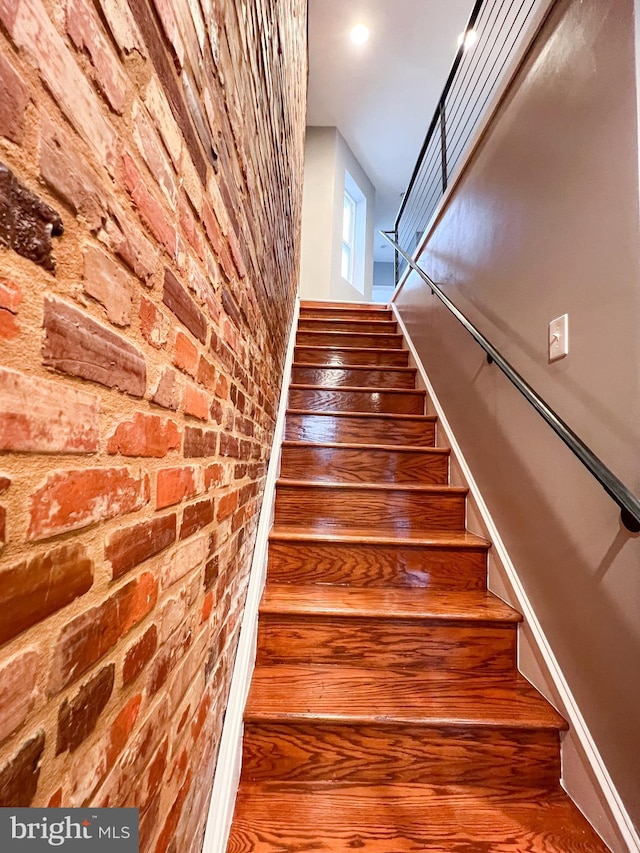 stairway featuring brick wall and wood finished floors