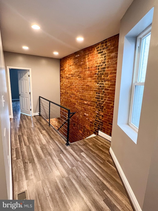 hallway featuring wood finished floors, an upstairs landing, baseboards, and brick wall