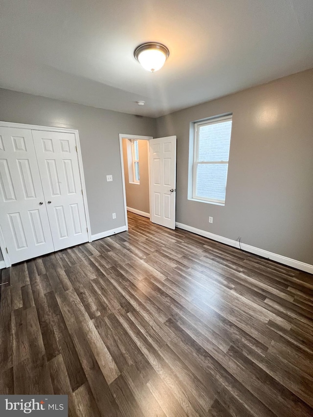 unfurnished bedroom with dark wood finished floors, a closet, and baseboards