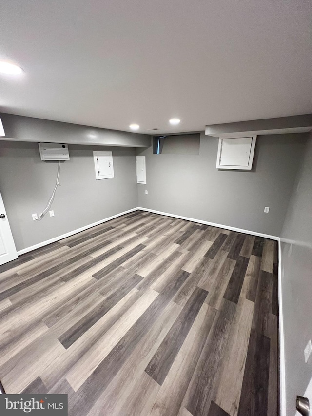 finished below grade area featuring an AC wall unit, recessed lighting, wood finished floors, and baseboards