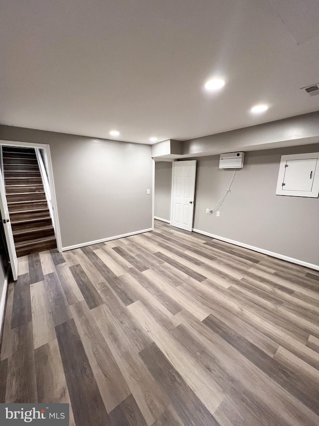 finished below grade area with baseboards, stairs, a wall unit AC, recessed lighting, and wood finished floors