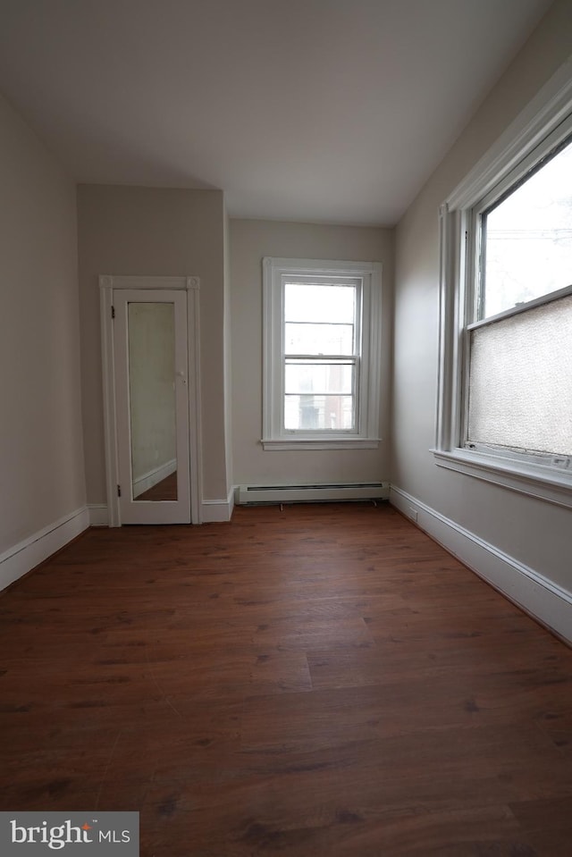 unfurnished room featuring baseboard heating and dark wood-type flooring