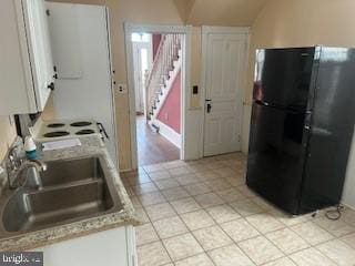 kitchen featuring sink, white cabinets, and black fridge