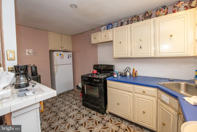 kitchen with tasteful backsplash, sink, white refrigerator, gas stove, and cream cabinetry