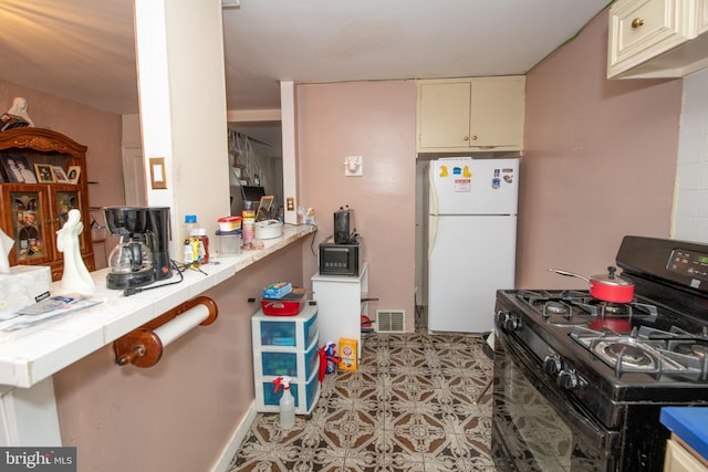 kitchen with white refrigerator, tile counters, black range with gas stovetop, and cream cabinetry