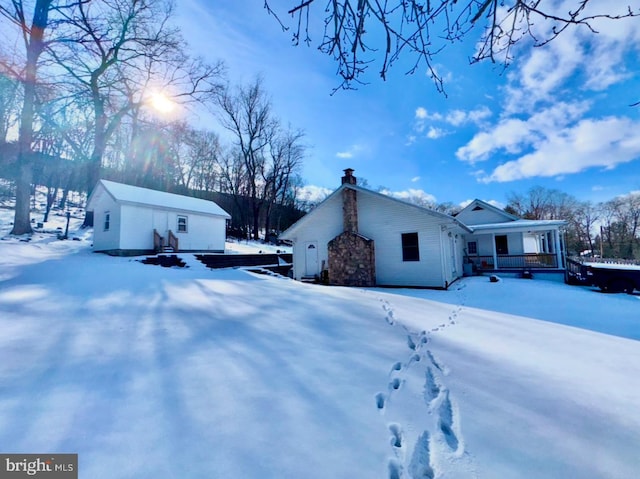 view of snow covered exterior featuring an outbuilding and a porch