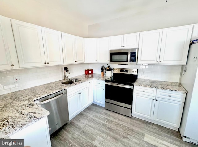 kitchen featuring appliances with stainless steel finishes, sink, white cabinets, light stone counters, and light hardwood / wood-style floors