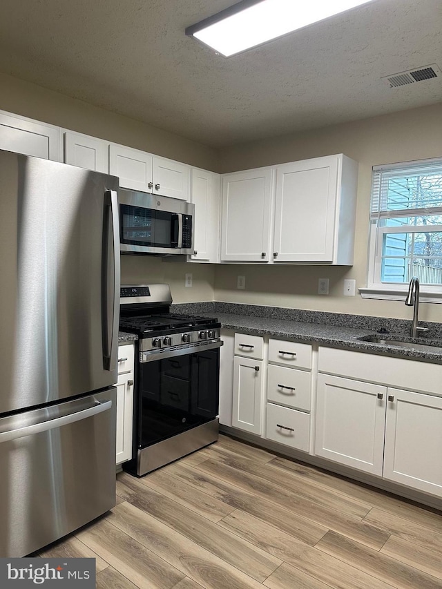 kitchen featuring appliances with stainless steel finishes, sink, light wood-type flooring, white cabinets, and a textured ceiling