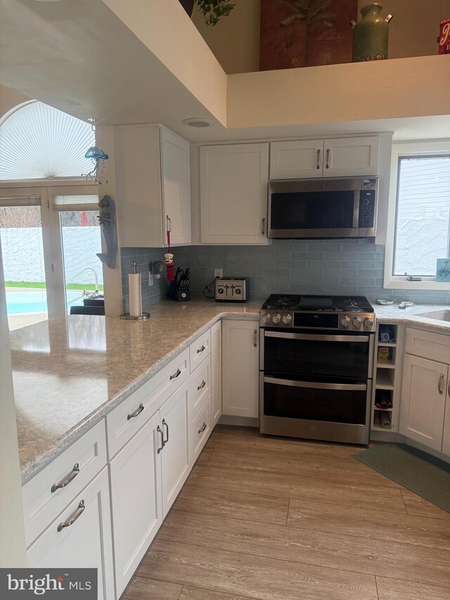 kitchen with stainless steel appliances, light stone countertops, light hardwood / wood-style floors, and white cabinets