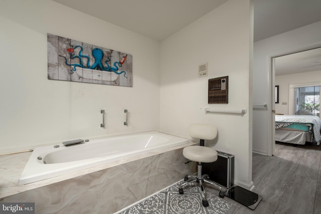 bathroom with a relaxing tiled tub and hardwood / wood-style flooring