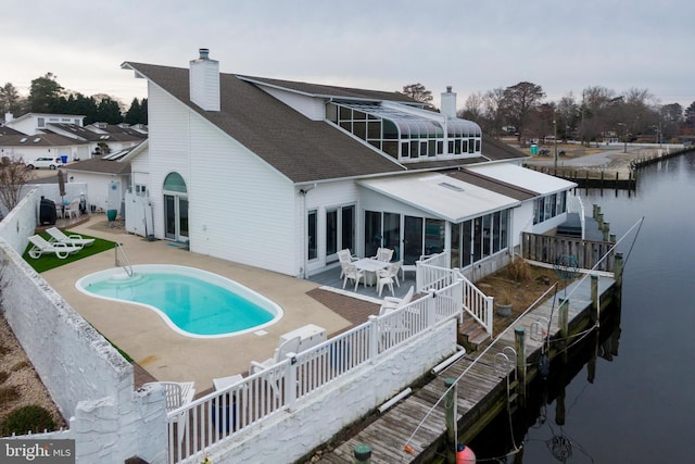 rear view of property featuring a water view, a patio, a sunroom, and a fenced in pool