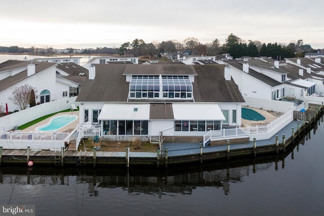 back of property with a fenced in pool, a sunroom, and a water view