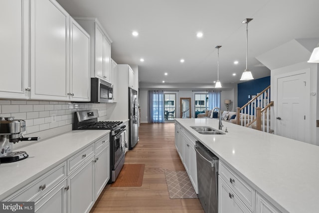 kitchen with sink, white cabinetry, stainless steel appliances, decorative light fixtures, and light wood-type flooring