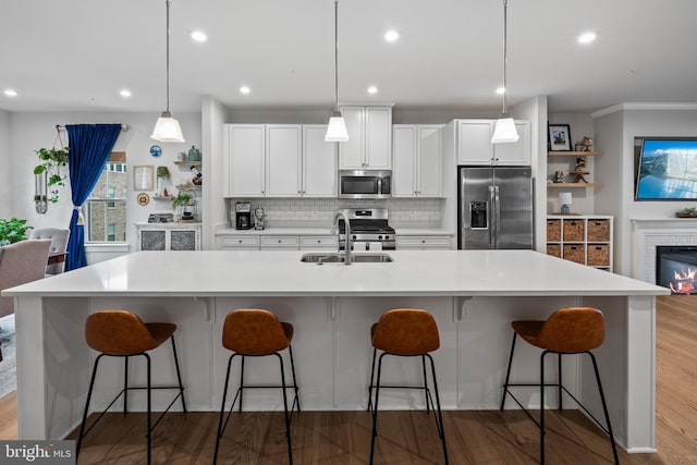 kitchen with sink, hanging light fixtures, stainless steel appliances, white cabinets, and a large island with sink