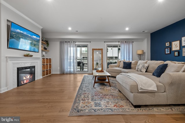 living room featuring a tile fireplace, ornamental molding, and light hardwood / wood-style flooring