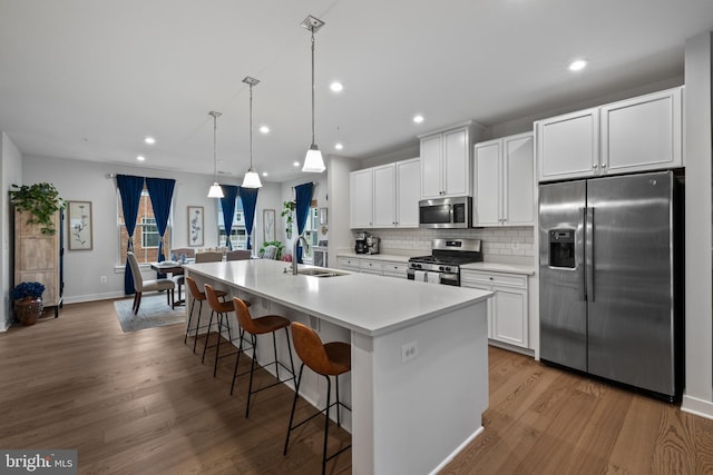 kitchen featuring appliances with stainless steel finishes, decorative light fixtures, sink, white cabinets, and a center island with sink