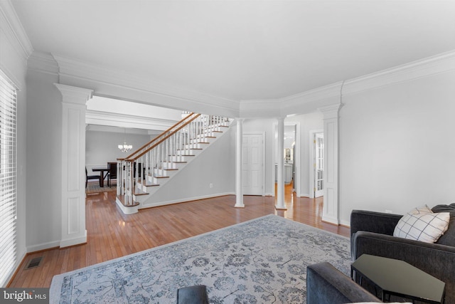 living room featuring decorative columns, wood-type flooring, ornamental molding, and an inviting chandelier