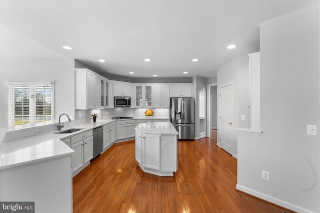 kitchen with a kitchen island, wood-type flooring, sink, white cabinets, and stainless steel appliances