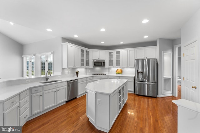 kitchen with a kitchen island, appliances with stainless steel finishes, white cabinetry, sink, and light hardwood / wood-style floors