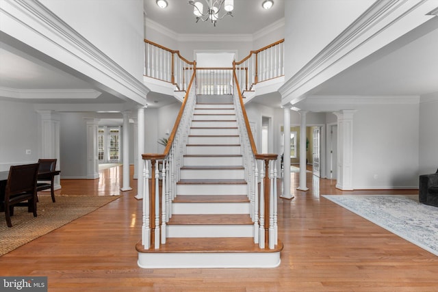 staircase with hardwood / wood-style flooring, ornamental molding, a high ceiling, and ornate columns