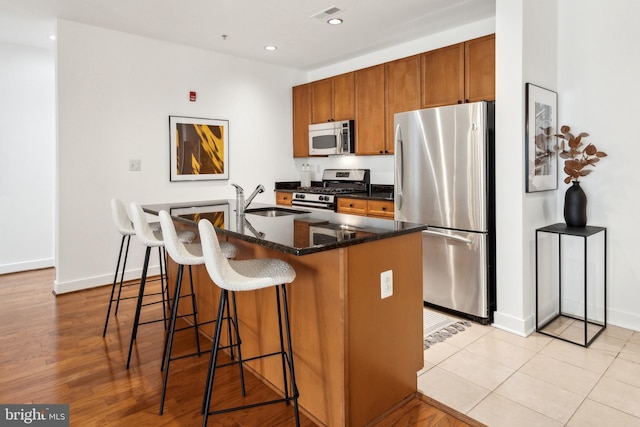 kitchen with sink, a breakfast bar, dark stone countertops, stainless steel appliances, and a center island with sink