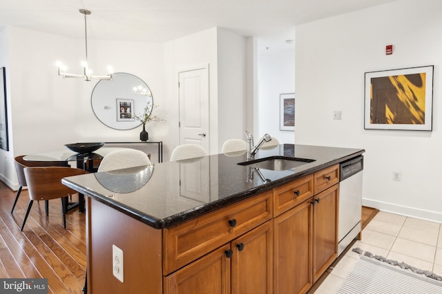 kitchen with sink, decorative light fixtures, stainless steel dishwasher, an island with sink, and dark stone counters