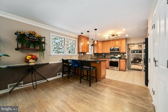 kitchen featuring a kitchen bar, crown molding, kitchen peninsula, stainless steel appliances, and decorative backsplash