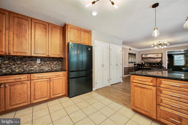 kitchen with black refrigerator, pendant lighting, backsplash, dark stone counters, and light tile patterned floors