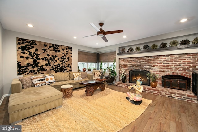 living room with ceiling fan, wood-type flooring, and a brick fireplace