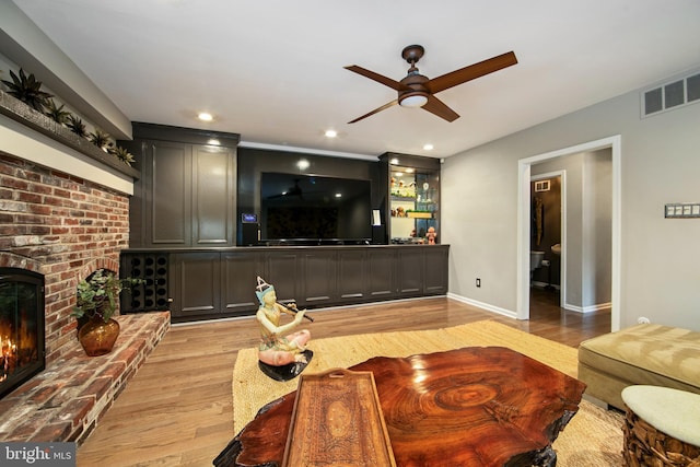 living room featuring a brick fireplace, ceiling fan, and light hardwood / wood-style flooring