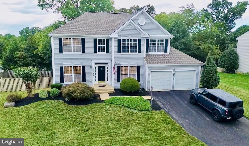 colonial house featuring a front lawn, fence, aphalt driveway, and roof with shingles