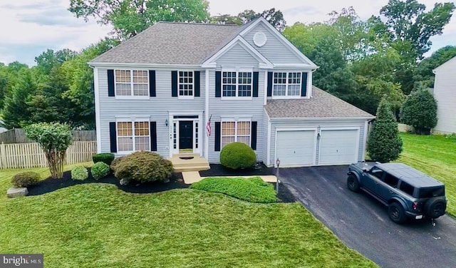 colonial house featuring a front lawn, fence, aphalt driveway, and roof with shingles