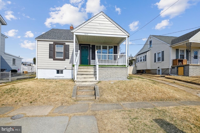 bungalow-style home featuring a shingled roof, fence, a front yard, covered porch, and a chimney