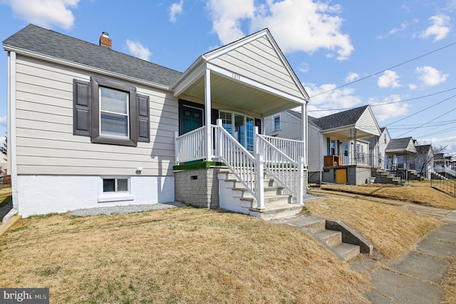 view of front of house with a shingled roof, a front lawn, stairway, covered porch, and a chimney