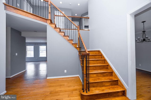 stairway with a towering ceiling, wood-type flooring, and a notable chandelier