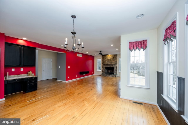 living room featuring a stone fireplace, ceiling fan with notable chandelier, and light hardwood / wood-style floors