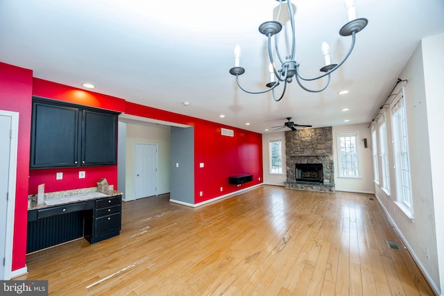 kitchen featuring light stone counters, ceiling fan, a stone fireplace, and light wood-type flooring