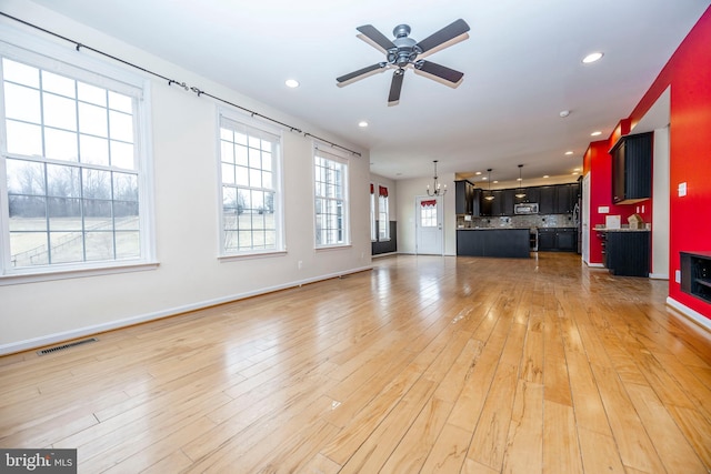 unfurnished living room with ceiling fan with notable chandelier and light hardwood / wood-style floors