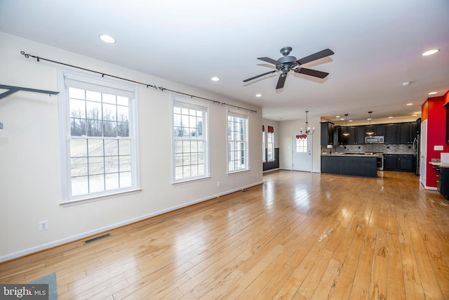 unfurnished living room with ceiling fan with notable chandelier and light wood-type flooring