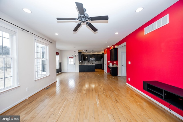 unfurnished living room with ceiling fan with notable chandelier and light hardwood / wood-style flooring