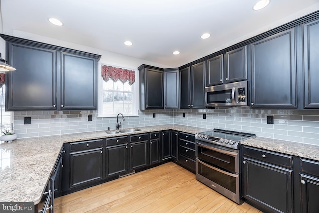 kitchen with sink, light stone counters, tasteful backsplash, stainless steel appliances, and light hardwood / wood-style floors