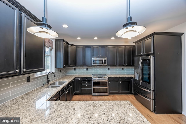 kitchen featuring pendant lighting, sink, decorative backsplash, stainless steel appliances, and light wood-type flooring