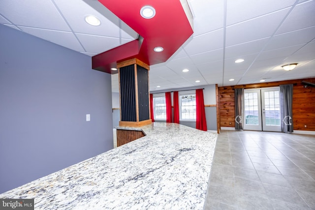 kitchen featuring light stone counters, a paneled ceiling, wood walls, and a wealth of natural light