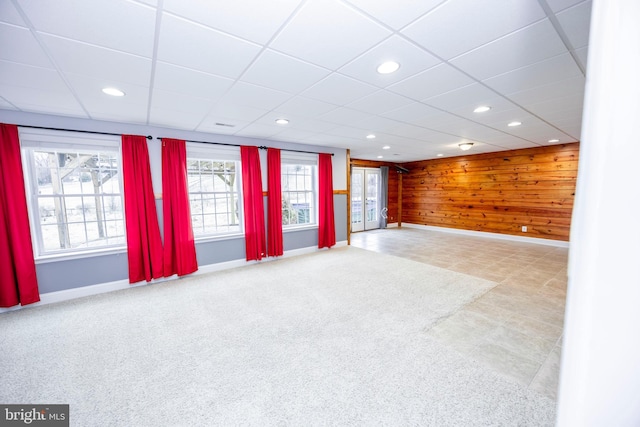 basement featuring carpet floors, a paneled ceiling, and wood walls