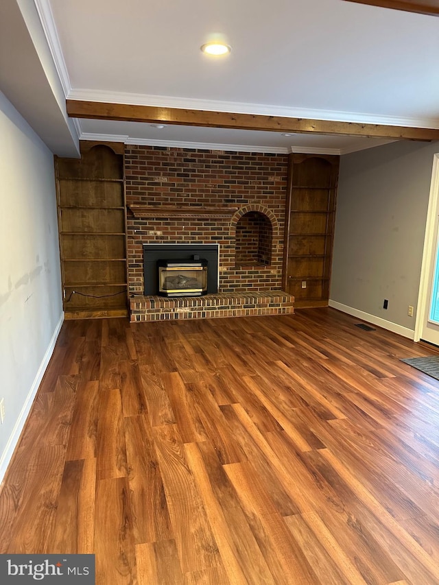 unfurnished living room with wood-type flooring, a brick fireplace, built in features, and crown molding