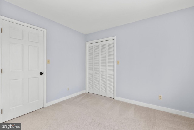 unfurnished bedroom featuring a closet, light colored carpet, and baseboards