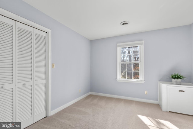 unfurnished bedroom with baseboards, visible vents, a closet, and light colored carpet