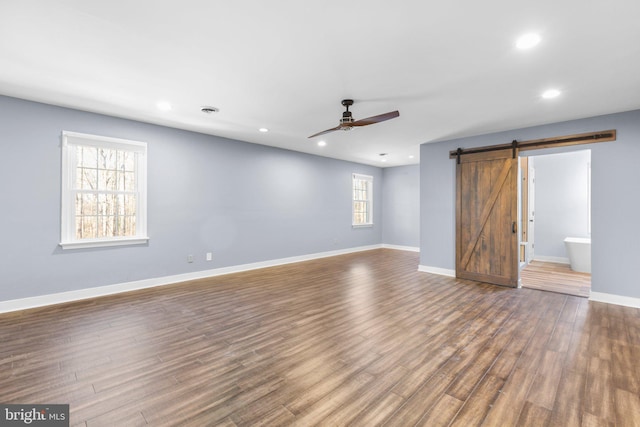 unfurnished living room featuring ceiling fan, dark wood finished floors, baseboards, and a barn door