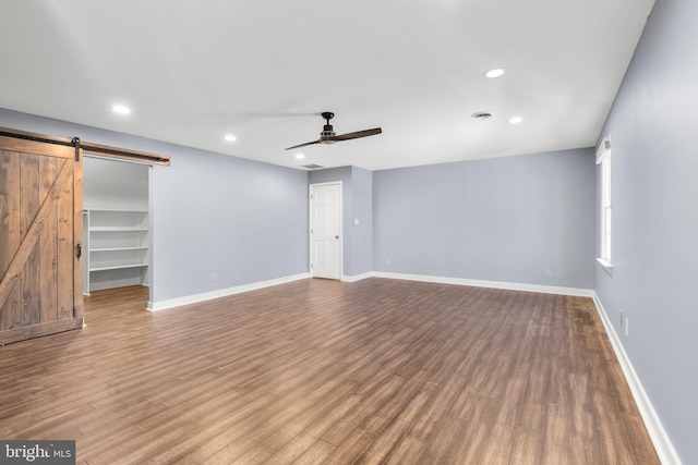 unfurnished living room with a ceiling fan, wood finished floors, baseboards, and a barn door