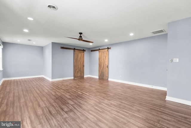 empty room featuring wood finished floors, visible vents, baseboards, and a barn door